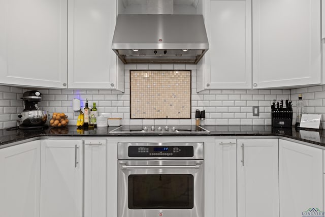 kitchen with wall chimney range hood, black electric stovetop, oven, white cabinetry, and decorative backsplash