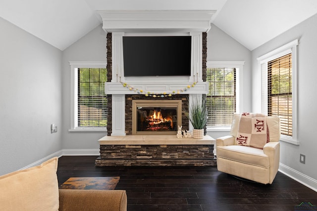 living area with plenty of natural light, dark wood-type flooring, lofted ceiling, and a stone fireplace