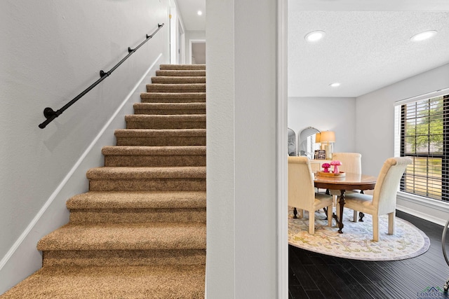 stairway featuring baseboards, recessed lighting, a textured ceiling, and wood finished floors