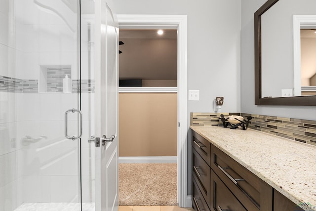 bathroom featuring vanity, baseboards, a stall shower, and backsplash