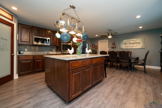 kitchen with appliances with stainless steel finishes, ceiling fan, pendant lighting, hardwood / wood-style floors, and a kitchen island