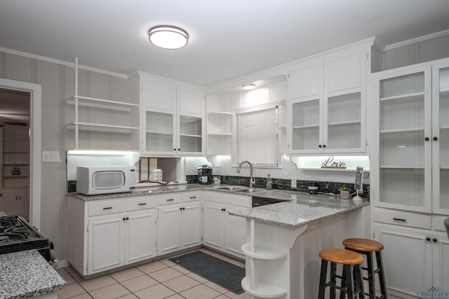 kitchen with white microwave, white cabinetry, open shelves, light stone countertops, and a sink