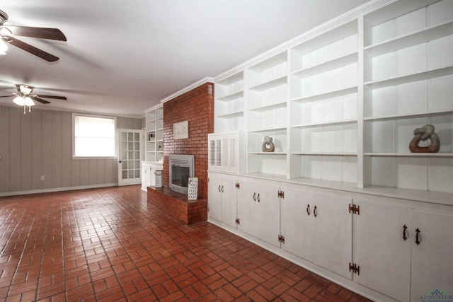unfurnished living room featuring wood walls, a fireplace, brick floor, and a ceiling fan