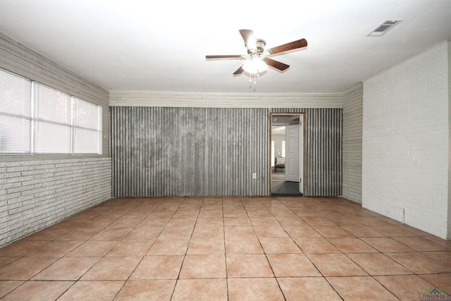 empty room featuring brick wall, light tile patterned flooring, a ceiling fan, and visible vents