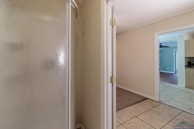 hallway featuring light tile patterned floors, crown molding, baseboards, and light colored carpet
