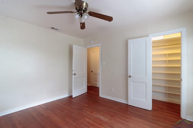 unfurnished bedroom with a walk in closet, visible vents, wood finished floors, baseboards, and a closet