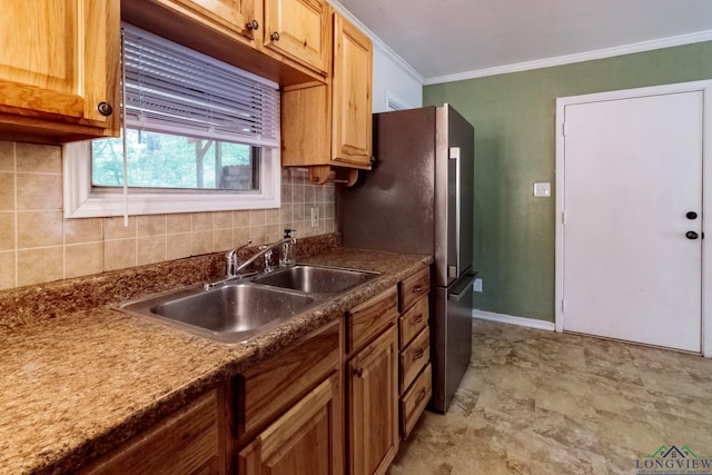 kitchen with a sink, tasteful backsplash, freestanding refrigerator, and crown molding
