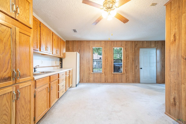 kitchen featuring wood walls, light carpet, white refrigerator, sink, and ceiling fan