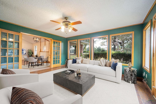 living room with wood-type flooring, ceiling fan with notable chandelier, a textured ceiling, and crown molding