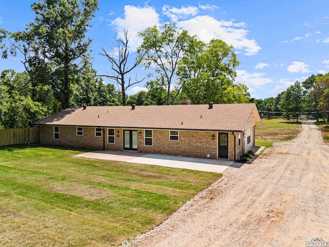 view of front facade with brick siding, dirt driveway, a patio area, fence, and a front lawn