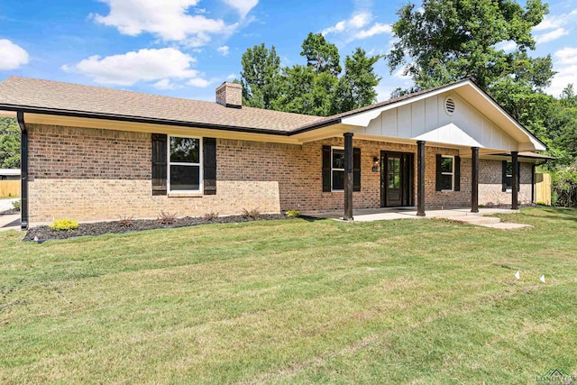 ranch-style home featuring brick siding, a shingled roof, a front lawn, a chimney, and a patio area