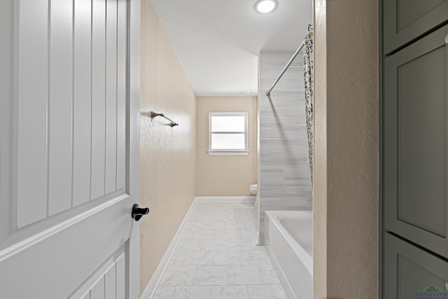 full bathroom featuring a textured wall, marble finish floor, and toilet