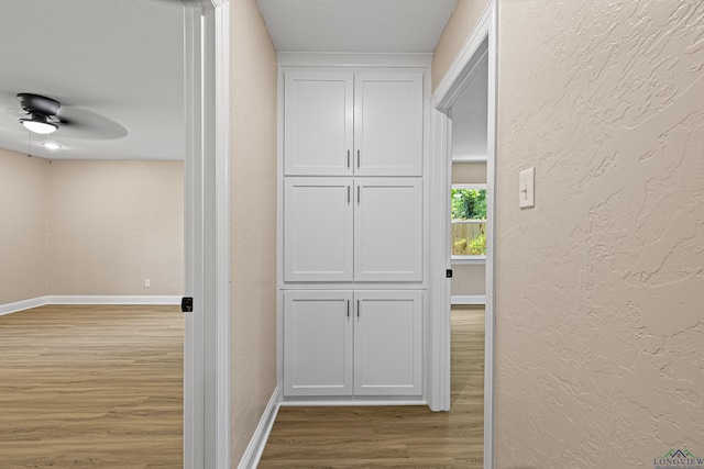 corridor featuring light wood-type flooring, baseboards, and a textured wall