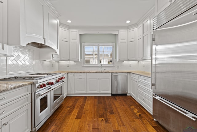 kitchen with sink, dark wood-type flooring, white cabinetry, premium appliances, and light stone countertops