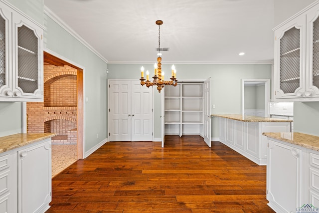 unfurnished dining area featuring a fireplace, ornamental molding, dark hardwood / wood-style flooring, and a chandelier