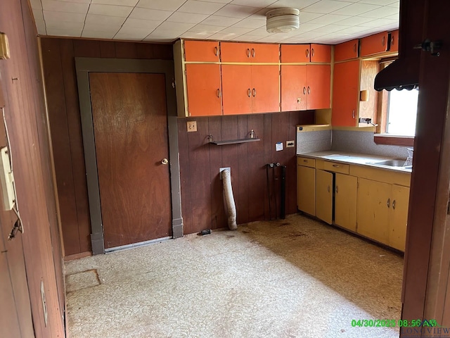 kitchen featuring a sink, light countertops, yellow cabinets, and wooden walls