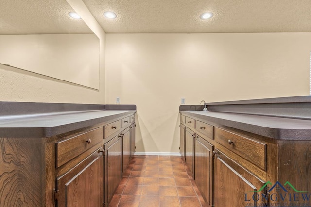 bar featuring sink, dark tile patterned floors, a textured ceiling, and dark brown cabinetry