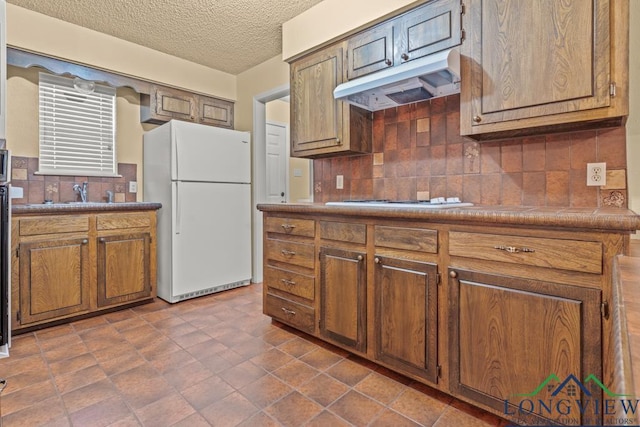 kitchen with a textured ceiling, white appliances, tasteful backsplash, and sink