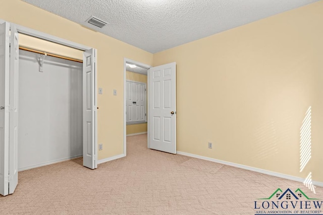 unfurnished bedroom with a textured ceiling, light colored carpet, and a closet