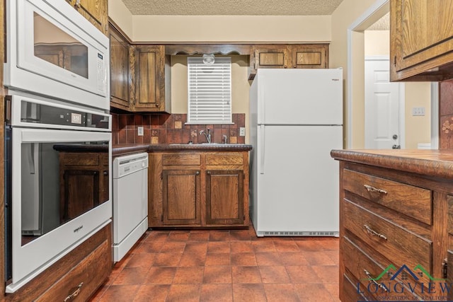 kitchen with a textured ceiling, white appliances, sink, and tasteful backsplash