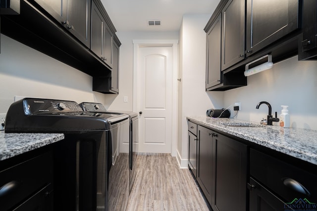 washroom featuring washing machine and clothes dryer, light hardwood / wood-style flooring, cabinets, and sink