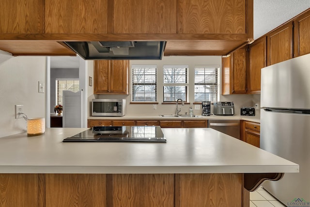 kitchen featuring light countertops, appliances with stainless steel finishes, brown cabinetry, and a sink