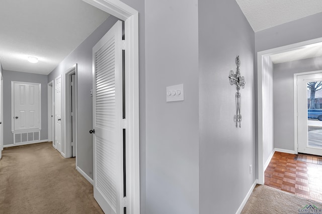 hall with carpet, visible vents, a textured ceiling, and baseboards