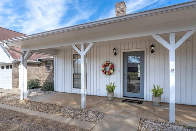 view of exterior entry with covered porch, a shingled roof, a chimney, and brick siding