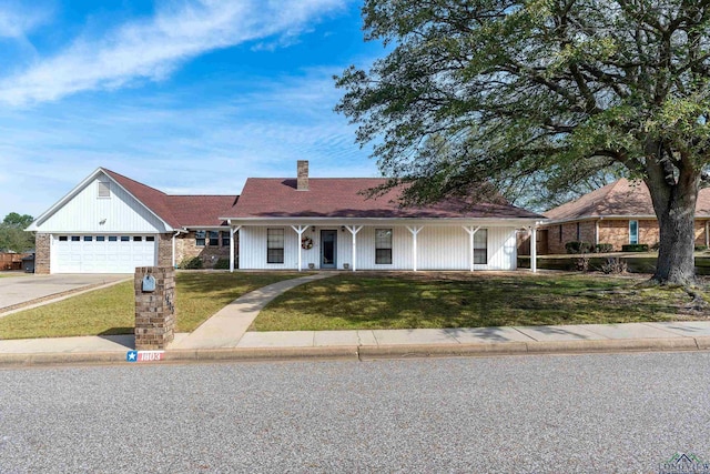 view of front of house featuring an attached garage, covered porch, concrete driveway, a chimney, and a front yard