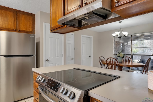 kitchen with a chandelier, under cabinet range hood, light countertops, appliances with stainless steel finishes, and brown cabinets