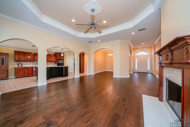 unfurnished living room featuring a raised ceiling, light hardwood / wood-style flooring, ceiling fan with notable chandelier, and ornamental molding