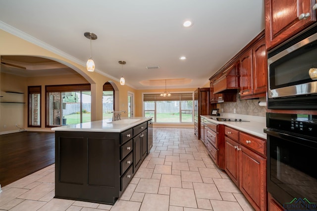 kitchen featuring a kitchen island with sink, black appliances, sink, hanging light fixtures, and a tray ceiling