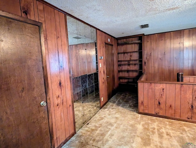 corridor featuring visible vents, crown molding, wood walls, carpet flooring, and a textured ceiling