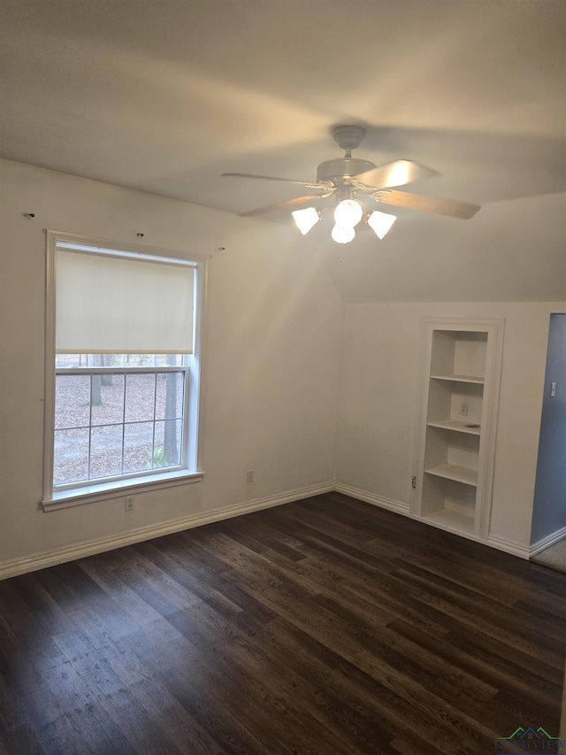 spare room featuring lofted ceiling, built in shelves, dark hardwood / wood-style floors, and ceiling fan