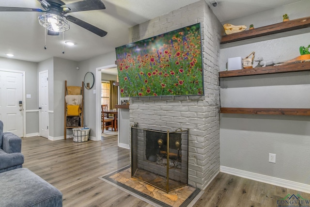 living area featuring a brick fireplace, a ceiling fan, baseboards, and wood finished floors