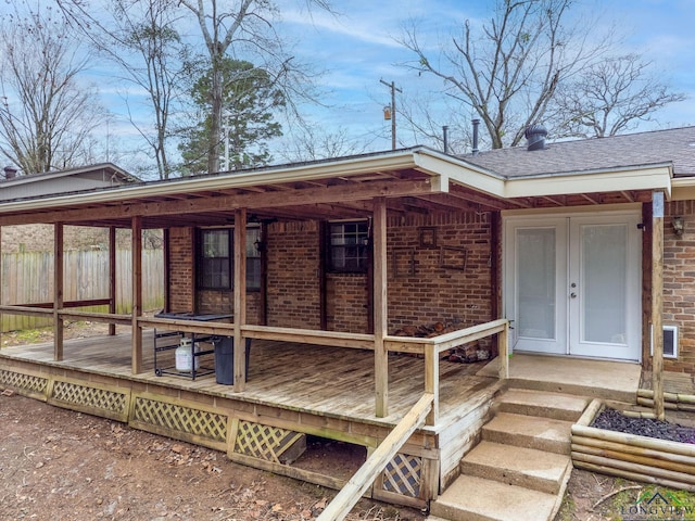 view of exterior entry with brick siding, fence, and roof with shingles