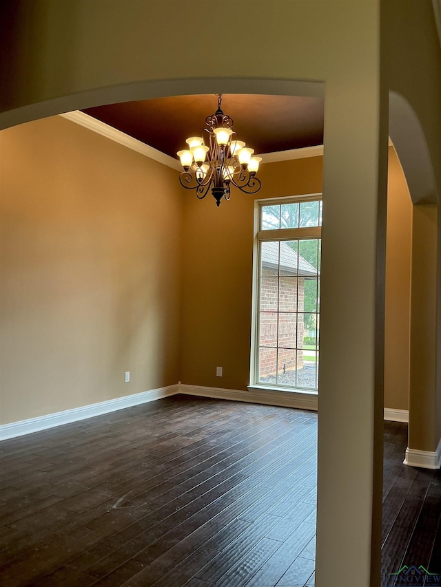empty room with dark wood-style flooring, baseboards, arched walkways, a chandelier, and ornamental molding