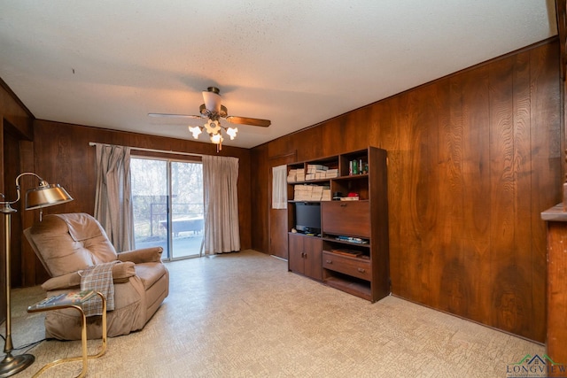 sitting room featuring ceiling fan, a textured ceiling, and wood walls