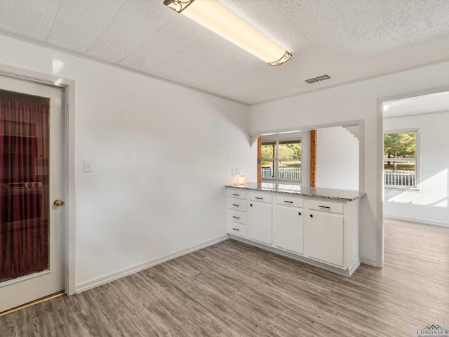 kitchen featuring a wealth of natural light, white cabinets, ornamental molding, and light wood-type flooring