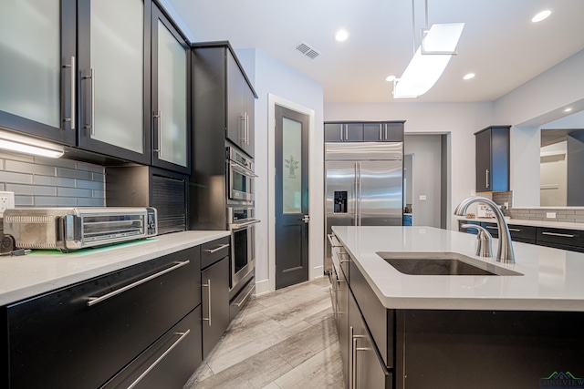 kitchen with sink, pendant lighting, a kitchen island with sink, and backsplash