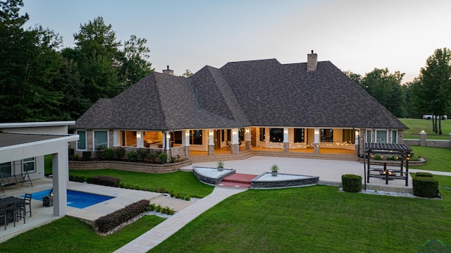 back house at dusk featuring a lawn and a patio area