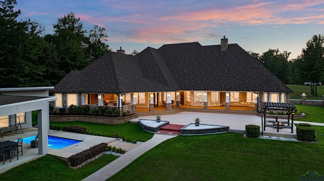 back house at dusk with a patio and a lawn