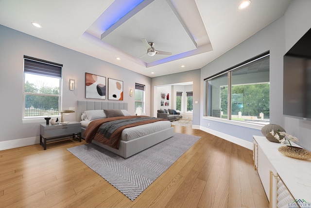 bedroom with ceiling fan, a tray ceiling, and light wood-type flooring