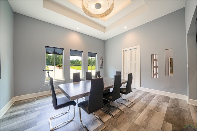 dining room with a tray ceiling, a towering ceiling, and light wood-type flooring