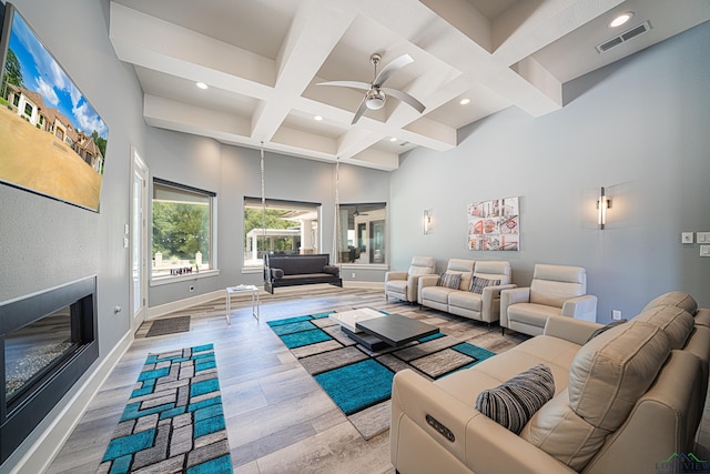 living room featuring a towering ceiling, coffered ceiling, ceiling fan, beam ceiling, and light hardwood / wood-style flooring