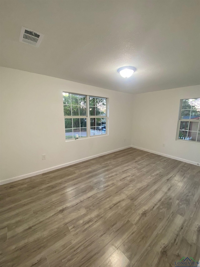 unfurnished room with dark wood-type flooring, a healthy amount of sunlight, visible vents, and baseboards