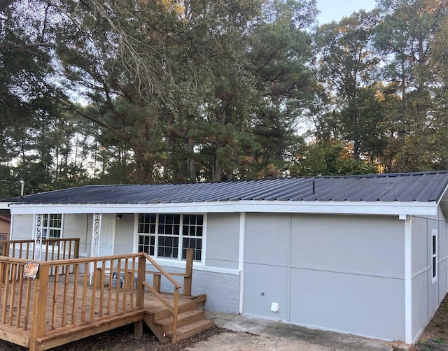 single story home featuring metal roof, brick siding, and a wooden deck