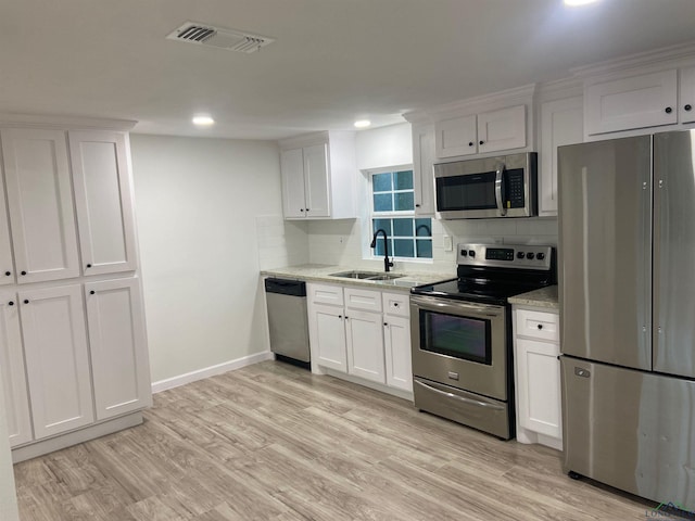 kitchen featuring light stone countertops, stainless steel appliances, light wood-style floors, white cabinetry, and a sink