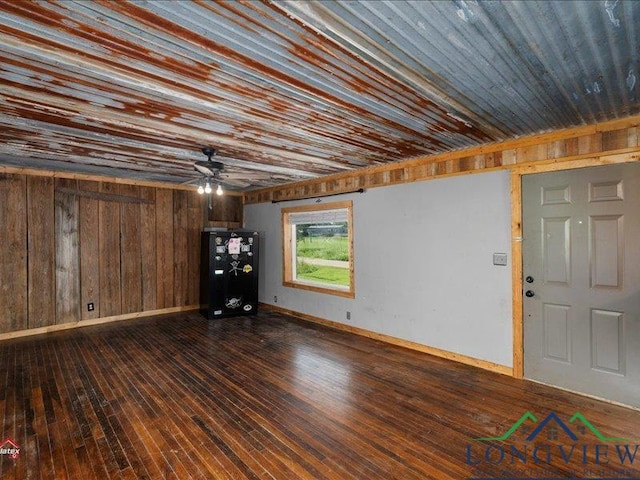 interior space with dark hardwood / wood-style floors, ceiling fan, and wood walls