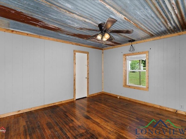 spare room featuring ceiling fan, dark wood-type flooring, and wood walls